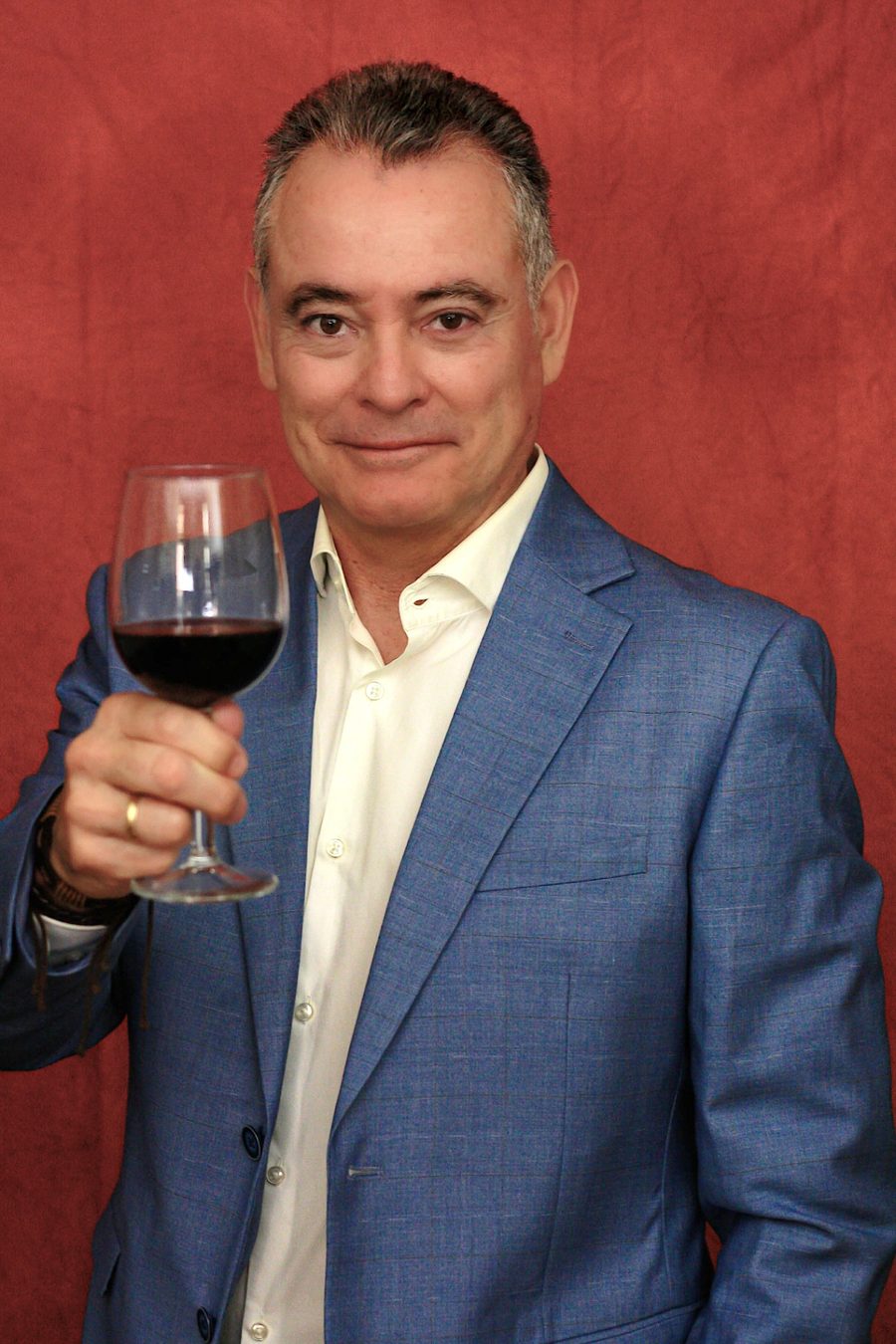 Retrato de Gabio Maggi con chaqueta azul, sosteniendo una copa de vino tinto sobre fondo rojo